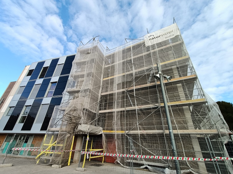 Fotografia 1. Vista de la nova façana modular prefabricada instal·lada en la primera fase de les obres (esquerra) i bastida per a les obres de la segona fase (dreta)